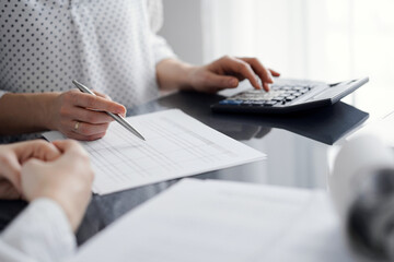 Woman accountant using a calculator and laptop computer while counting and discussing taxes with a client. Business audit and finance concepts