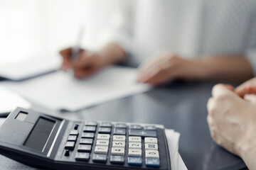 Woman accountant using a pen and laptop computer while counting and discussing taxes with a client, focus on the calculator. Business audit and finance concepts