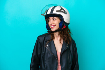 Young caucasian woman with a motorcycle helmet isolated on blue background looking to the side and smiling