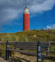 Fototapeta na wymiar Texel lighthouse on the hill with an empty wooden bench in the foreground