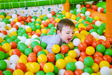 Fototapeta na wymiar Toddler baby plays in the pool with balls. Child boy crawling in the pool with plastic balls. Kid age one year nine months