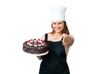 Middle age pastry chef woman holding a big cake over isolated background shaking hands for closing a good deal
