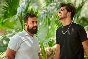 Two funny indian men laughing and speak Hindi in public park green palm leaves background, true...