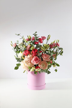 Beautiful bouquet in festive round box on white table.Pink box.Variety of flowers in the bouquet.Gift for a holiday, birthday, wedding, Mother's Day, Valentine's Day, Women's Day.Vertical photo.
