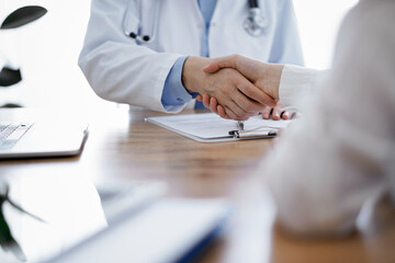 Doctor and patient shaking hands above the wooden table in clinic. Medicine concept