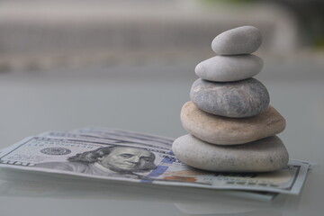 Pyramid of stones and euro banknotes. Stack of zen stones with hundred dollar bill on gray background. Rest on the sea.