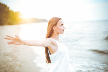 Fototapeta na wymiar Happy smiling woman in free happiness bliss on ocean beach standing with open hands. Portrait of a multicultural female model in white summer dress enjoying nature.