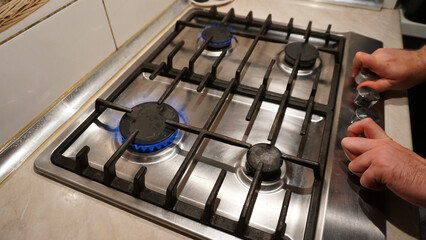 Turns off or turns on the gas on the stove. Blue flame of fire on black burners. The man's hands...