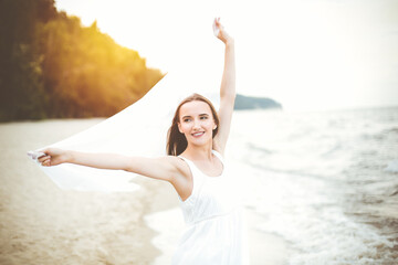 Happy smiling woman in free happiness bliss on ocean beach catching clouds. Portrait of a multicultural female model in white summer dress enjoying nature during travel holidays vacation outdoors