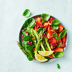 Spring salad with strawberries, pomegranate, asparagus, spinach, basil leaves and citrus-honey dressing. Top view