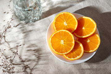 Sliced ripe oranges on plate and glass with water on table with aesthetic sunlight shadows, healthy...