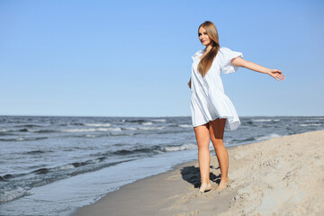 Fototapeta na wymiar Happy smiling beautiful woman is walking on the ocean beach with open arms