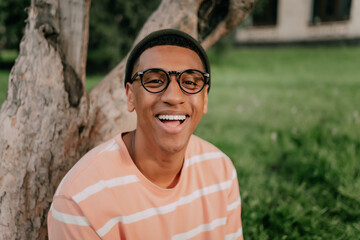 portrait of a stylish African man with glasses on the background of a city park smiling cheerfully and looking at the camera