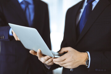 Business people discussing a presentation at meeting, standing in a modern office. Unknown businessman with a colleague search for some information at the laptop, lawyers at negotiation