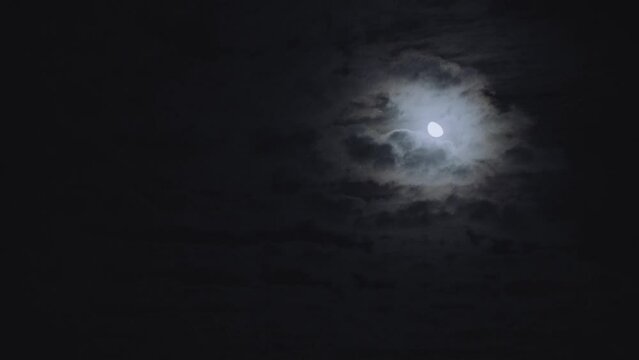 Scenic view of the moon shining between fluffy clouds in the dark sky at nighttime