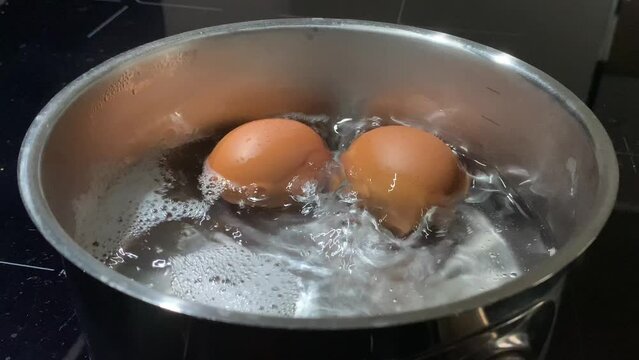 Chicken eggs in boiling water, close-up. Cooking food on an induction stove. Boiling water with chicken eggs in a saucepan.