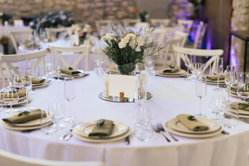 Round dining tables covered in white cloth and decorated with white flowers stand.