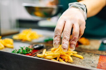 chef in cooking gloves serving french fries on wooden board.