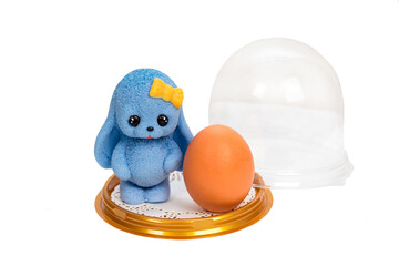 A rabbit with long ears and a handmade soap egg in a dome on a white background.
