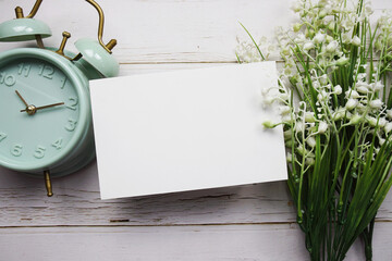 Empty card mockup with flower bouquet and alarm clock on wooden background