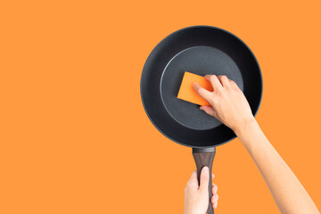 Female Hand Cleaning Frying Pan Isolated on Orange