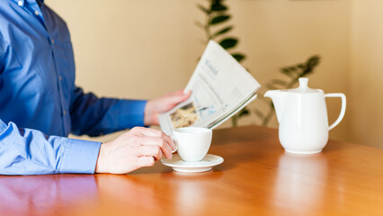 Ein Kaffee trinkender Mann sitzt am Tisch und liest Zeitung. - obrazy, fototapety, plakaty