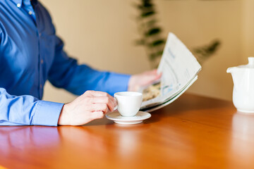 Ein Kaffee trinkender Mann sitzt am Tisch und liest Zeitung.