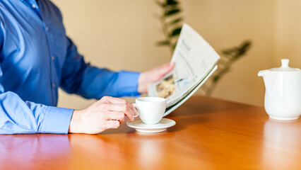Ein Kaffee trinkender Mann sitzt am Tisch und liest Zeitung.