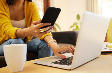 Closeup of woman working remote while typing on her laptop and holding her smartphone sitting on a...