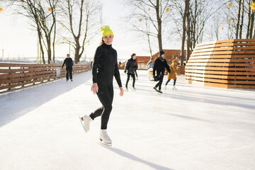 A woman in a yellow hat is skating on an ice rink in winter.