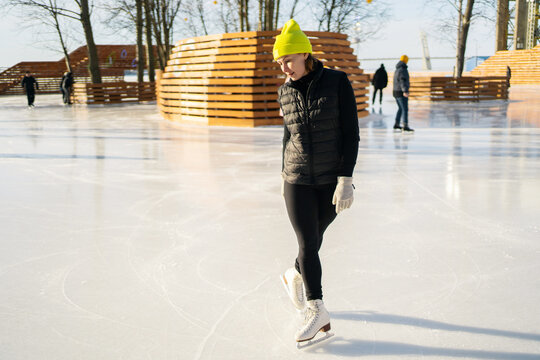 Lady learn to skate on ice. A man in a sports black uniform and a yellow hat. - Powered by Adobe