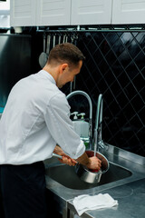 cheerful professional chef in the kitchen washing dirty dishes in the sink after cooking food...