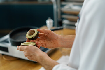 Professional kitchen chef cleans fresh green avocado with a knife removes the skin close-up