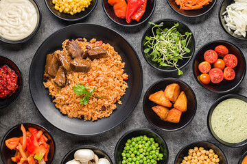 Rice with meat, vegetables and sauces on a dark stone background. View from above.
