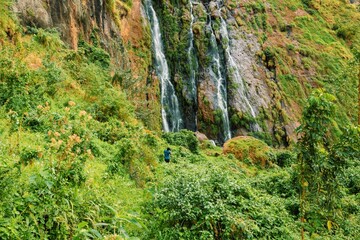 Rear view of a hiker against a waterfall in Wanale Hill in Mount Elgon, Mbale, Uganda