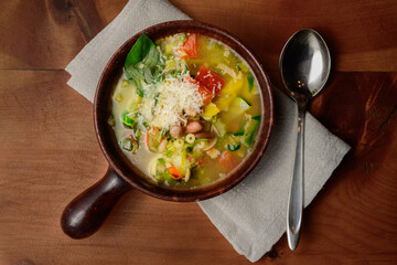 Minestrone Italian Vegetable Soup with Beans and Pasta in a Rustic Terracotta Bowl with Spoon and Napkin