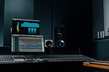 recording studio with a screen with sound wave and volume settings two subwoofers and a mixing console