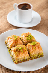 Pistachio baklava on a white plate with Turkish coffee.A plate of traditional baklava on burlap sack