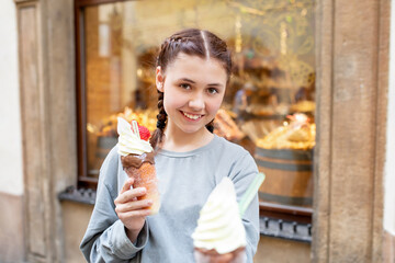 Happy teen girl with neatly braided hair with ice cream in a waffle cone outdoors, against the...