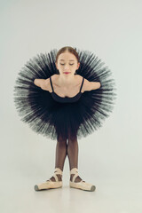ballerina in a black tutu is leaning forward with her arms crossed behind her back © Александр Иванов