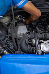 Fototapeta premium Close-up of a car mechanic changing oil in a mechanical workshop. Mechanic checking engine oil level in an auto car repair service center. A mechanics in uniform working in car repair and maintenance.