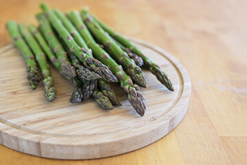 Fresh green asparagus on a cutting board and a wooden table, delicious spring time vegetables, copy space, selected focus