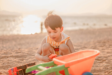 Kids playing on tropical beach. Children play at sea on summer family vacation. Sand and water toys, sun protection for young child. Little boy digging sand, building castle at ocean shore.

