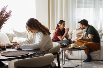 Young girl doing her home work while her parent are having a conversation behind her.