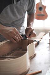 a man's hands perfecting the sides of a guitar under construction