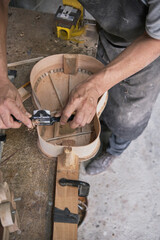 unrecognizable man shaving the sides of a guitar under construction