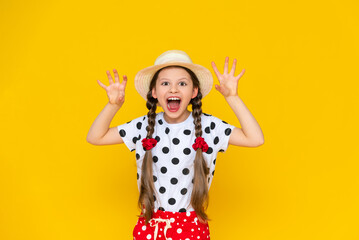 The child growls, portrays a beast with his mouth wide open. A little girl in a hat on a yellow isolated background parodies a predatory animal. Yellow isolated background.