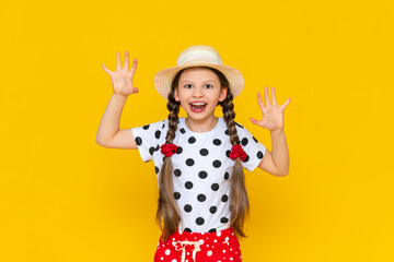 The child growls, portrays a beast with his mouth wide open. A little girl in a hat on a yellow isolated background parodies a predatory animal. Yellow isolated background.