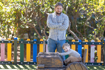 Father with his hands crossed and his little son on the playground