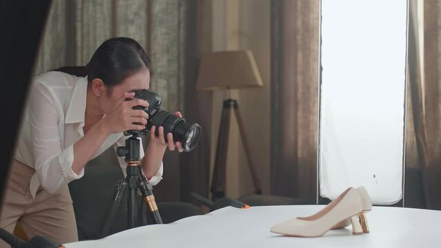 Asian Female Photographer Thinking About Women'S Shoes Position Then Raising Her Index Finger While Taking Photos Of Them In Home Studio 
